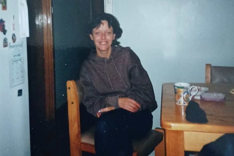 A woman is sitting at the kitchen table. He smiles.