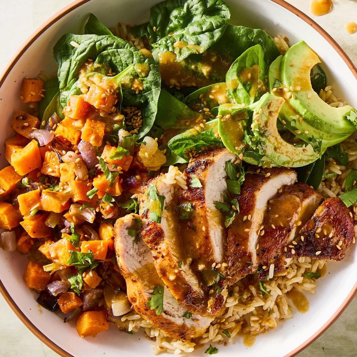 shredded chicken in a grain bowl with sweet potato, avocado, spinach and peanut dressing