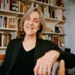 Rita Charon sits in a chair in front of a wall full of books on shelves