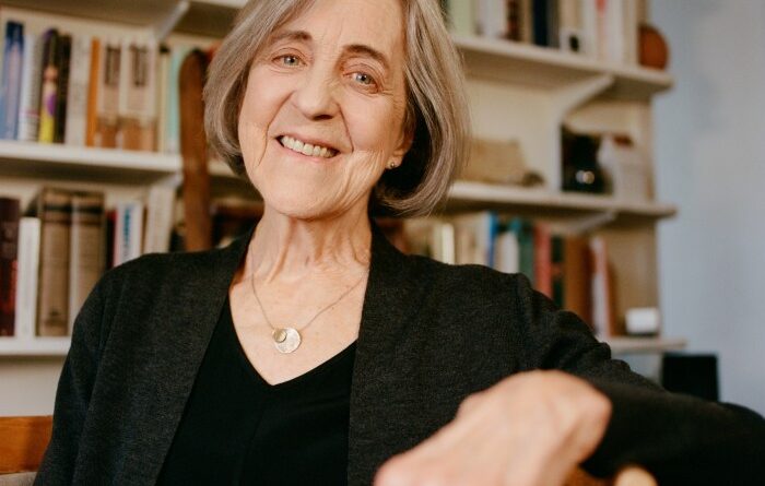 Rita Charon sits in a chair in front of a wall full of books on shelves